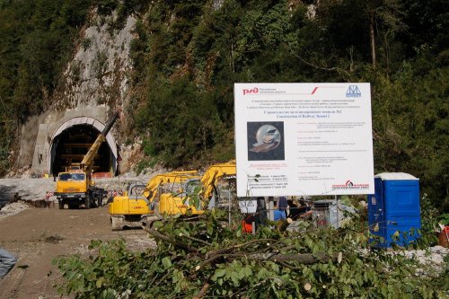 Порубочные остатки на фоне плаката, извещающего о том, что здесь ведется строительство тоннеля №2 совмещенной дороги